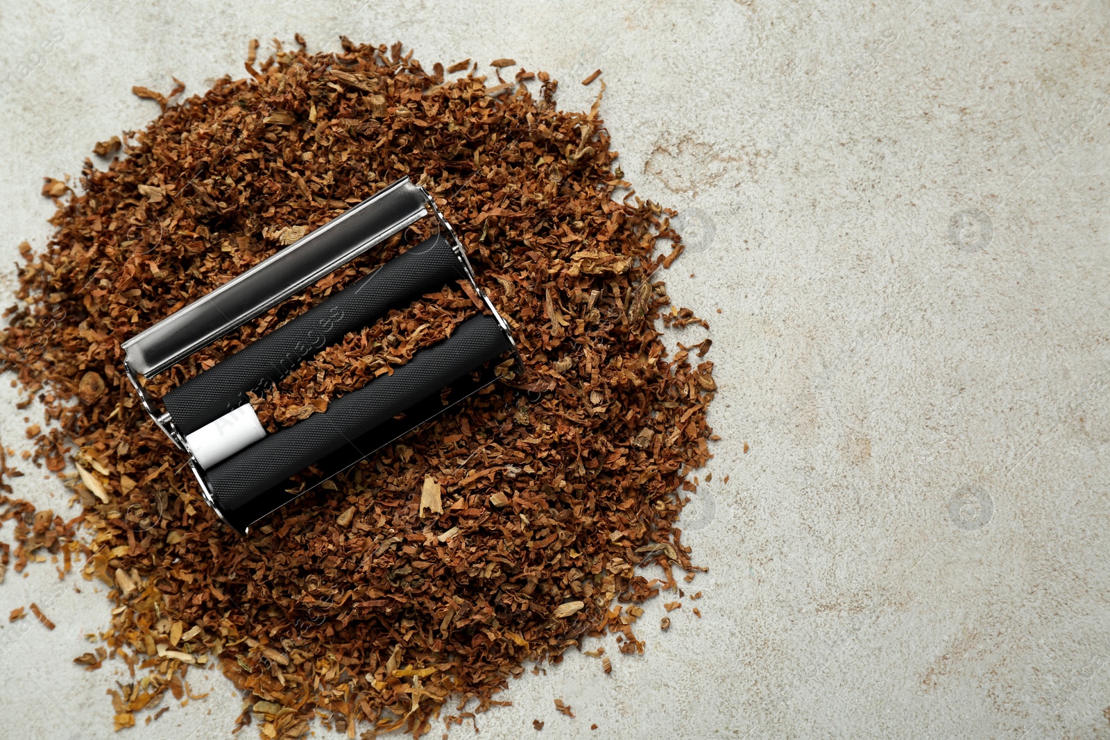 Photo of Making hand rolled cigarettes. Roller with filter and tobacco on light grey table, flat lay. Space for text