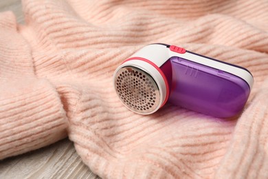 Photo of Modern fabric shaver for lint removing and sweater on wooden table