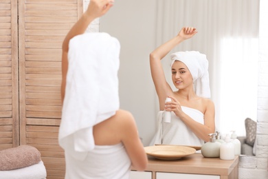 Photo of Beautiful young woman applying deodorant after shower in bathroom