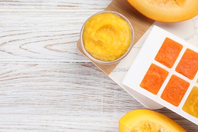 Different purees in ice cube tray ready for freezing and fresh pumpkin on white wooden table, flat lay. Space for text