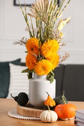 Photo of Beautiful bouquet with bright orange flowers and pumpkins on table indoors. Autumn vibes