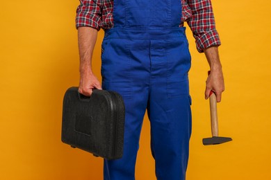 Photo of Professional builder in uniform with hammer and toolbox on yellow background