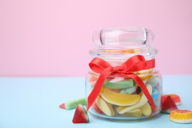 Photo of Glass jar with tasty colorful jelly candies on light blue table against pink background. Space for text