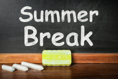 Chalk and duster on table near blackboard with inscription Summer Break. School holidays 
