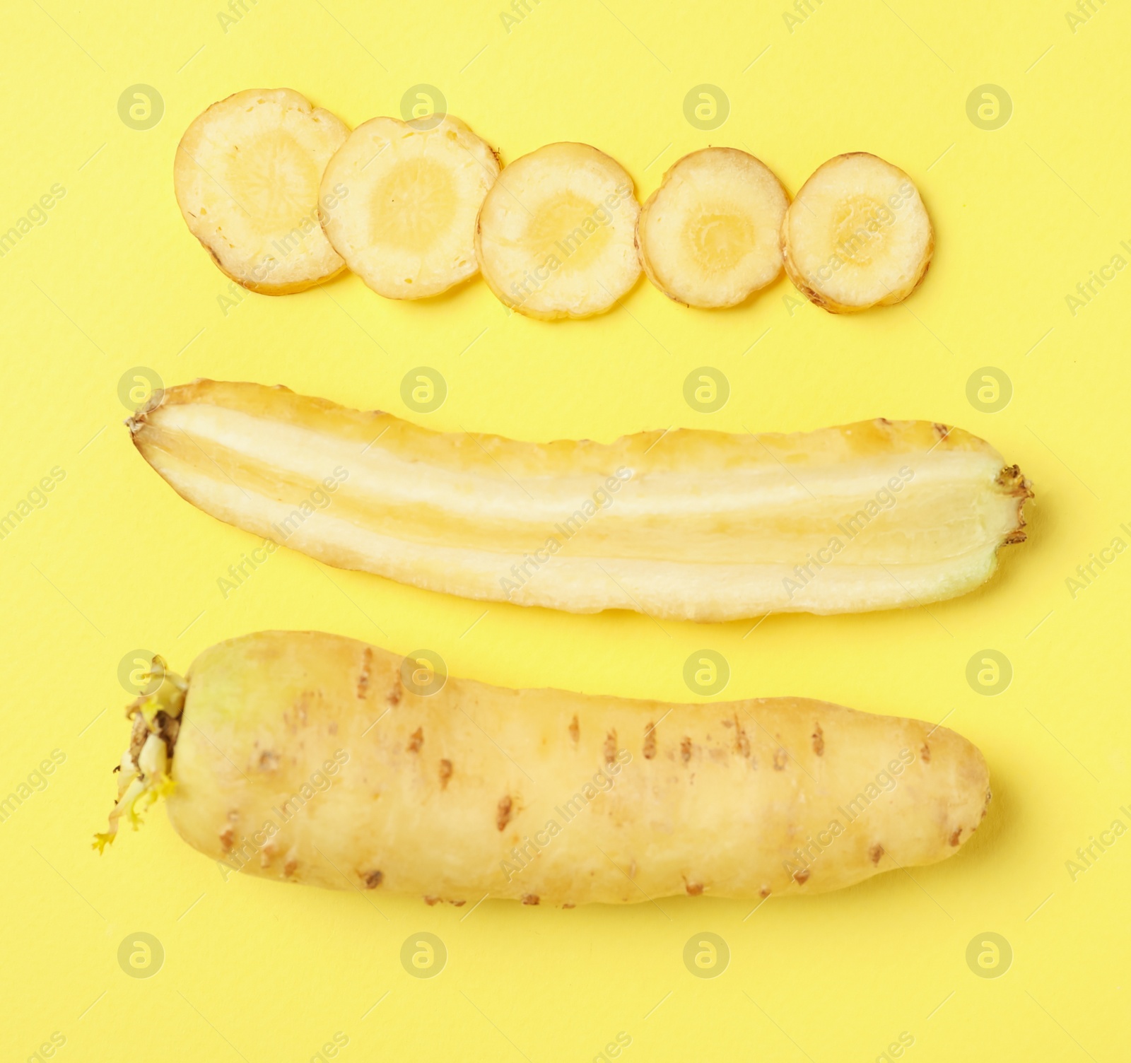 Photo of Whole and cut raw white carrots on yellow background, flat lay