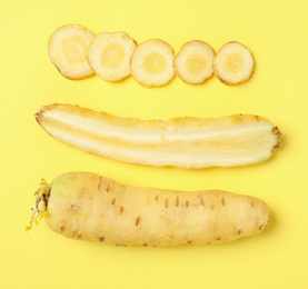 Photo of Whole and cut raw white carrots on yellow background, flat lay
