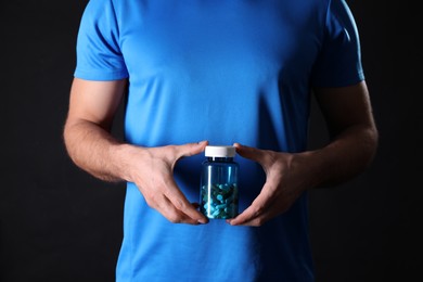 Photo of Man with bottle of pills on black background, closeup. Doping concept