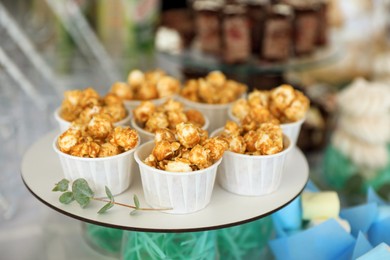 Cups with delicious caramel popcorn on dessert stand, closeup