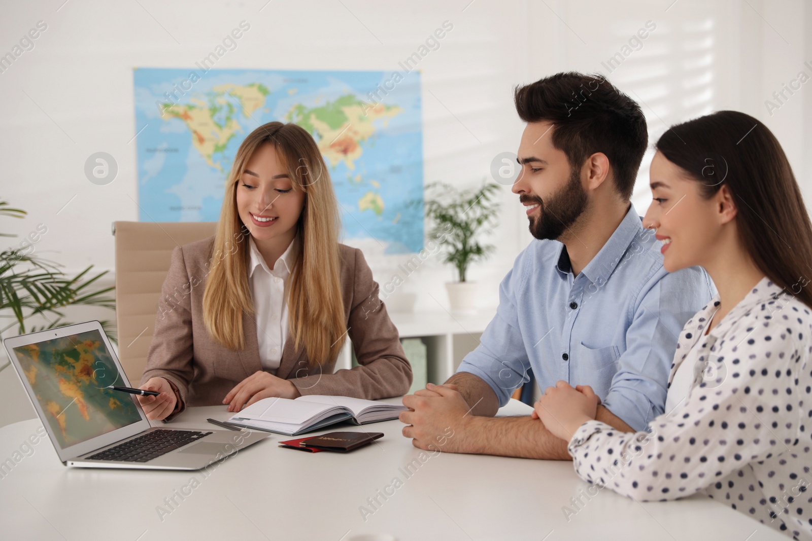 Photo of Manager showing map to couple on laptop at desk in travel agency