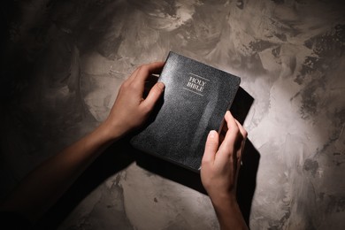 Religion. Christian woman praying over Bible at gray textured table, top view