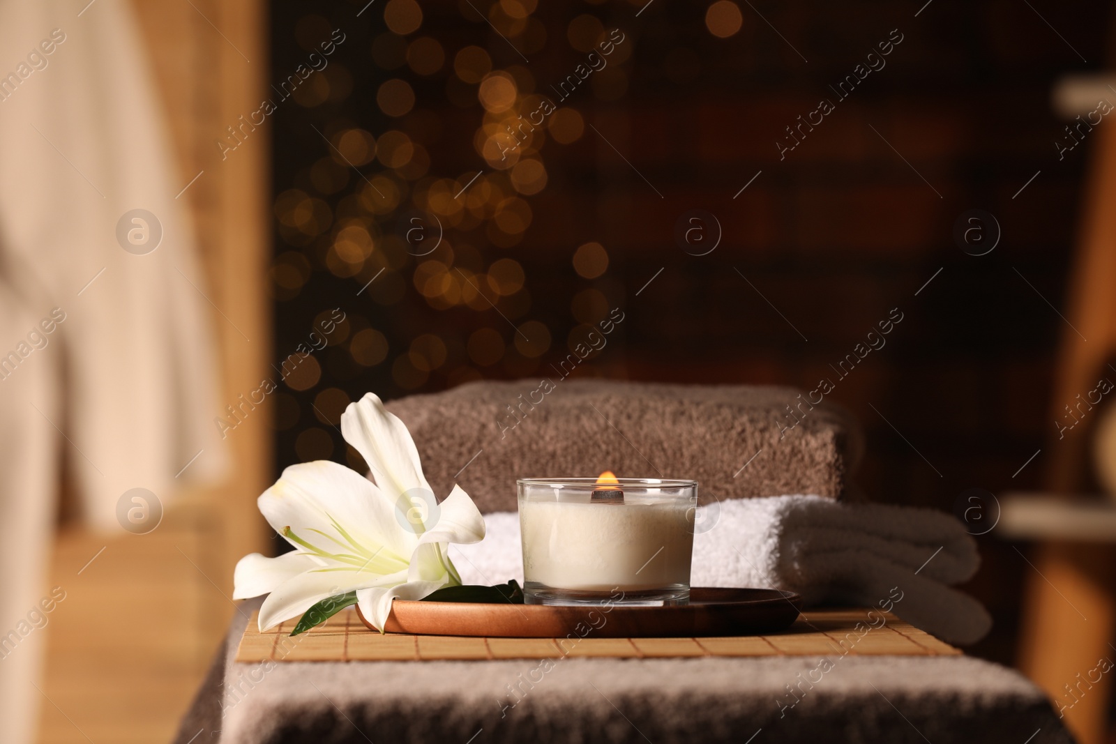 Photo of Spa composition with burning candle, lily flower and towels on massage table in wellness center, space for text