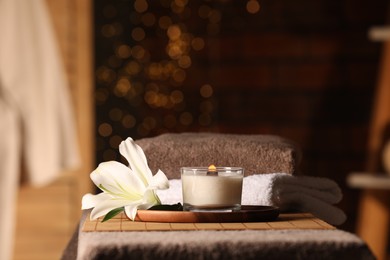 Photo of Spa composition with burning candle, lily flower and towels on massage table in wellness center, space for text