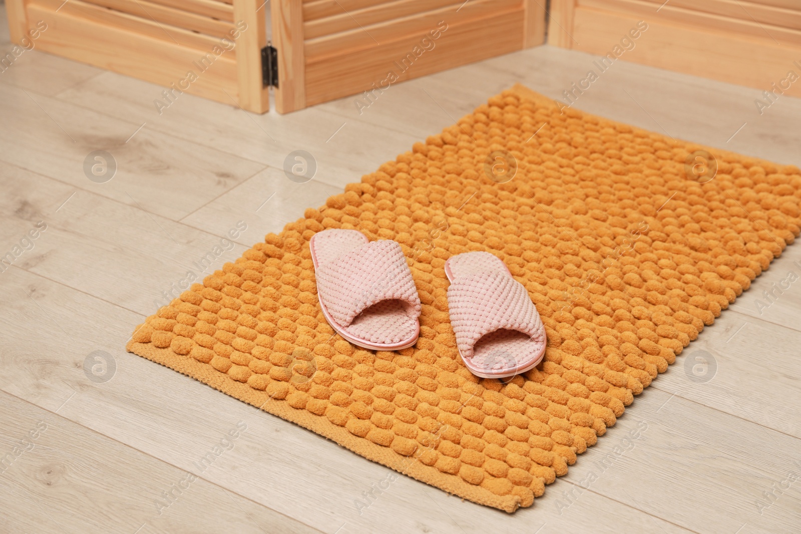 Photo of New yellow bath mat with soft slippers on floor indoors