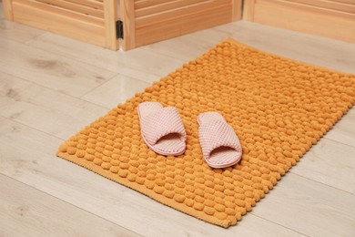 Photo of New yellow bath mat with soft slippers on floor indoors