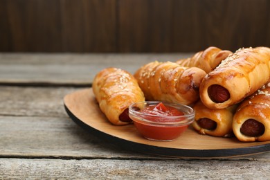 Photo of Delicious sausage rolls and ketchup on wooden table, closeup. Space for text