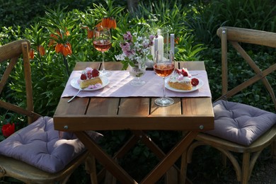 Photo of Vase with spring flowers, wine and cake on table served for romantic date in garden