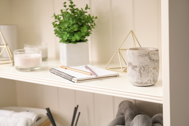 Photo of White shelving unit with notebook and different decorative stuff, closeup