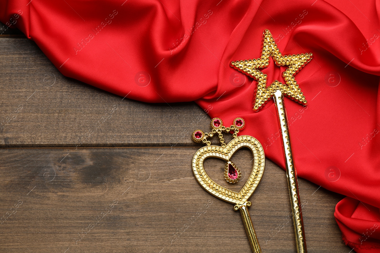 Photo of Different golden magic wands and red fabric on wooden table, flat lay. Space for text