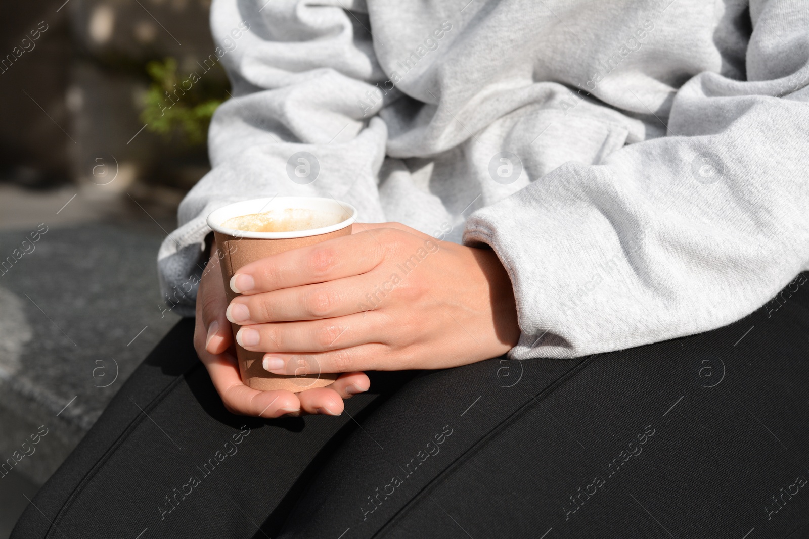 Photo of Woman sitting with cardboard cup of coffee outdoors, closeup