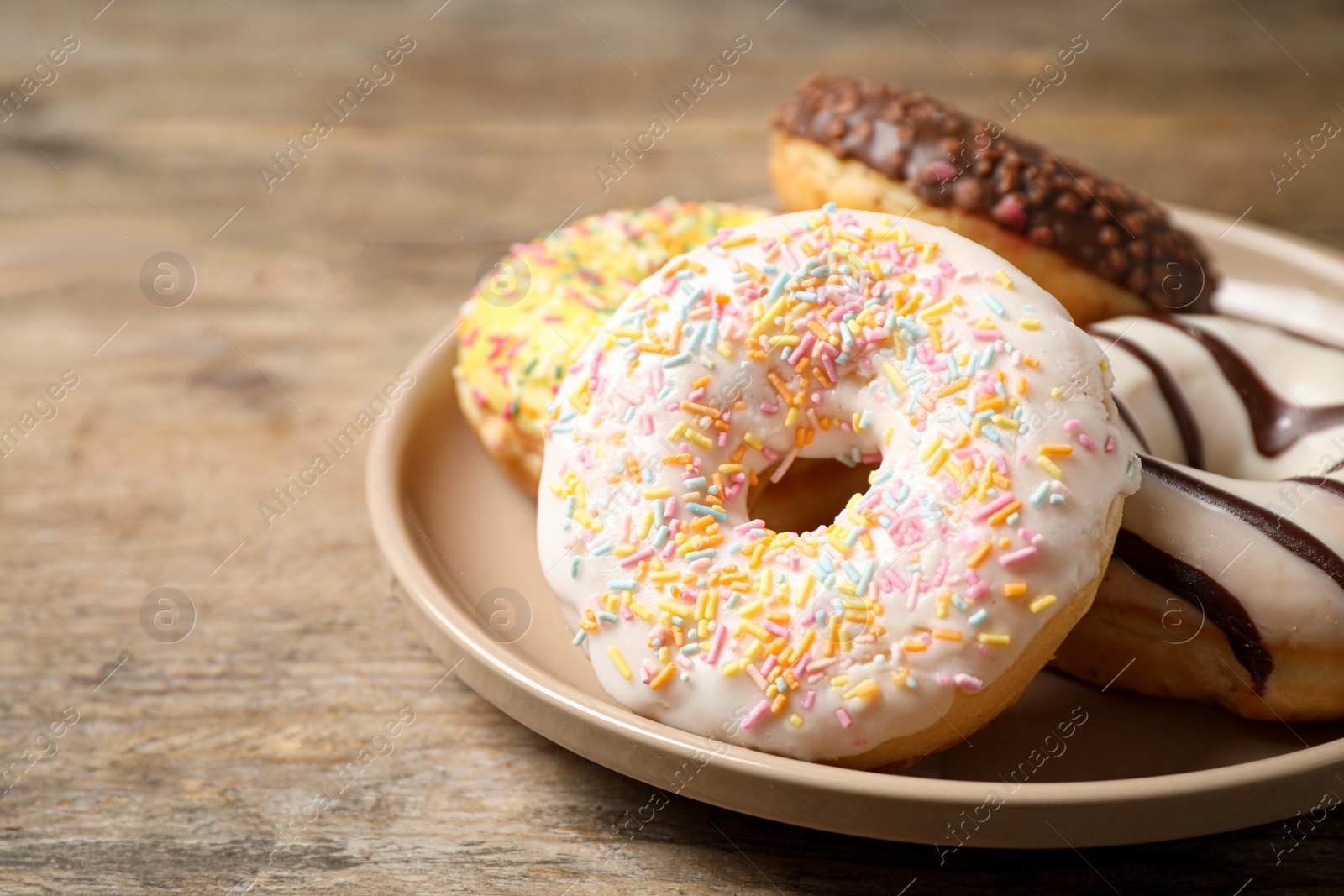 Photo of Delicious glazed donuts on wooden table, closeup