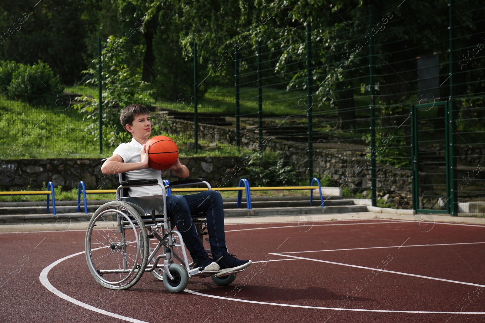 Photo of Disabled teenage boy in wheelchair playing basketball  on outdoor court