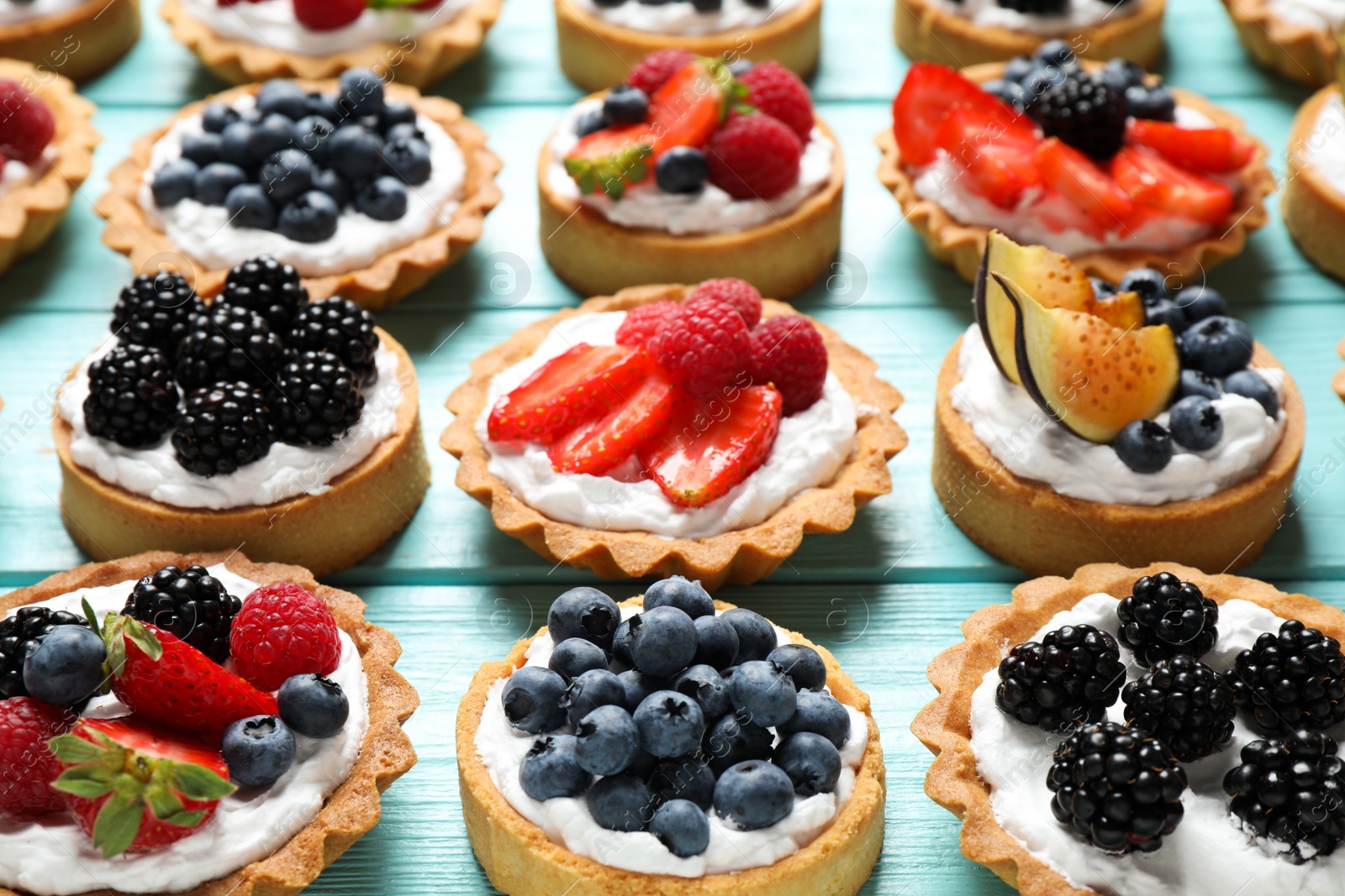 Photo of Many different berry tarts on blue wooden table. Delicious pastries