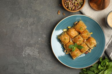 Photo of Delicious baklava with pistachios, nuts, mint and hot coffee on grey table, flat lay. Space for text