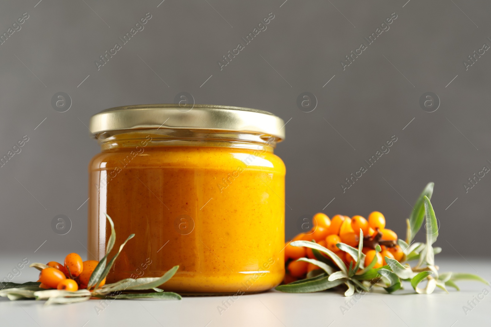 Photo of Delicious sea buckthorn jam and fresh berries on grey table. Space for text