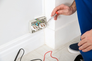 Photo of Electrician with neon-lamp tester checking voltage indoors, closeup