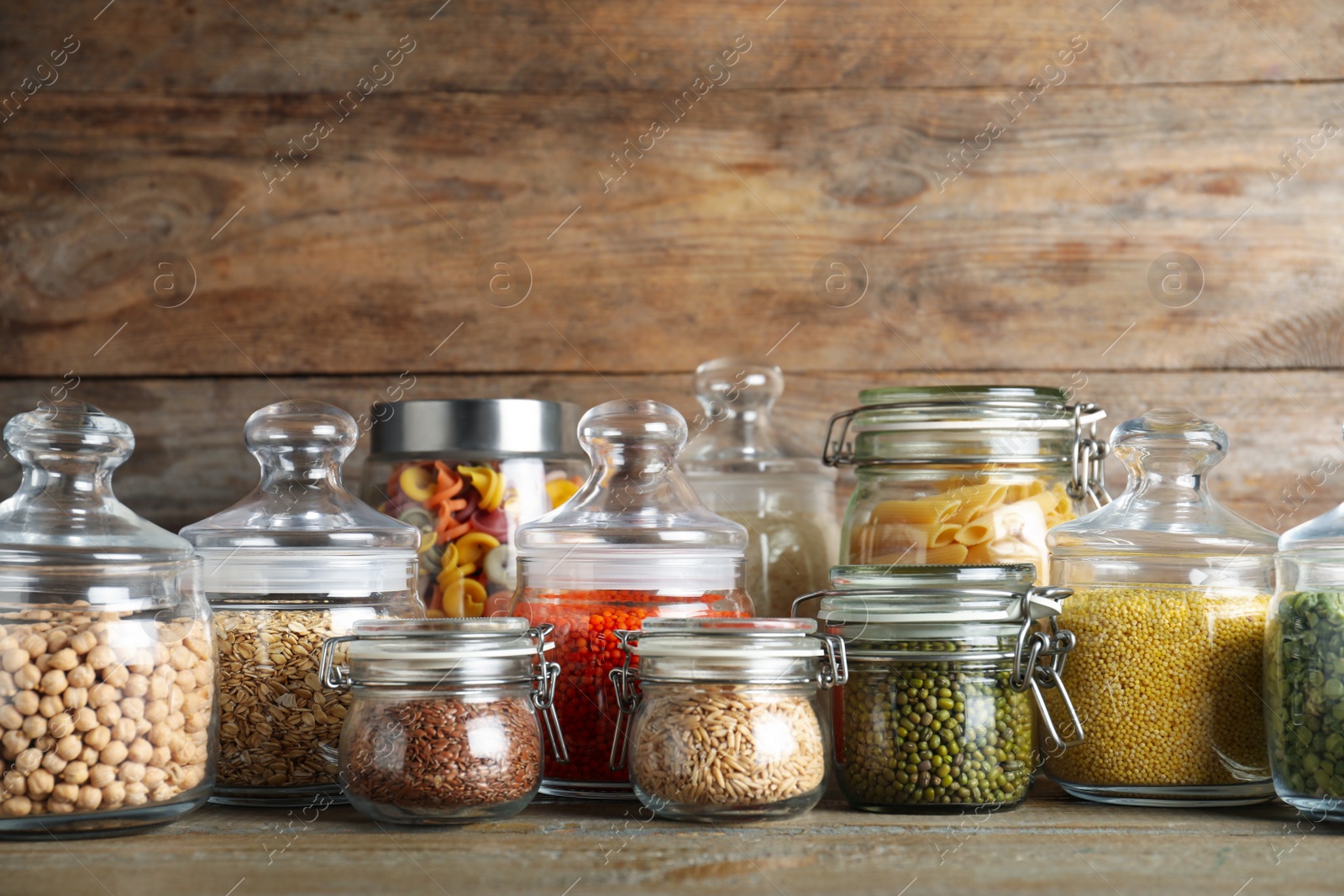 Photo of Glass jars with different types of groats and pasta on wooden table