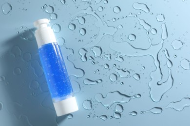 Bottle of cosmetic product and water drops on light blue background, top view. Space for text