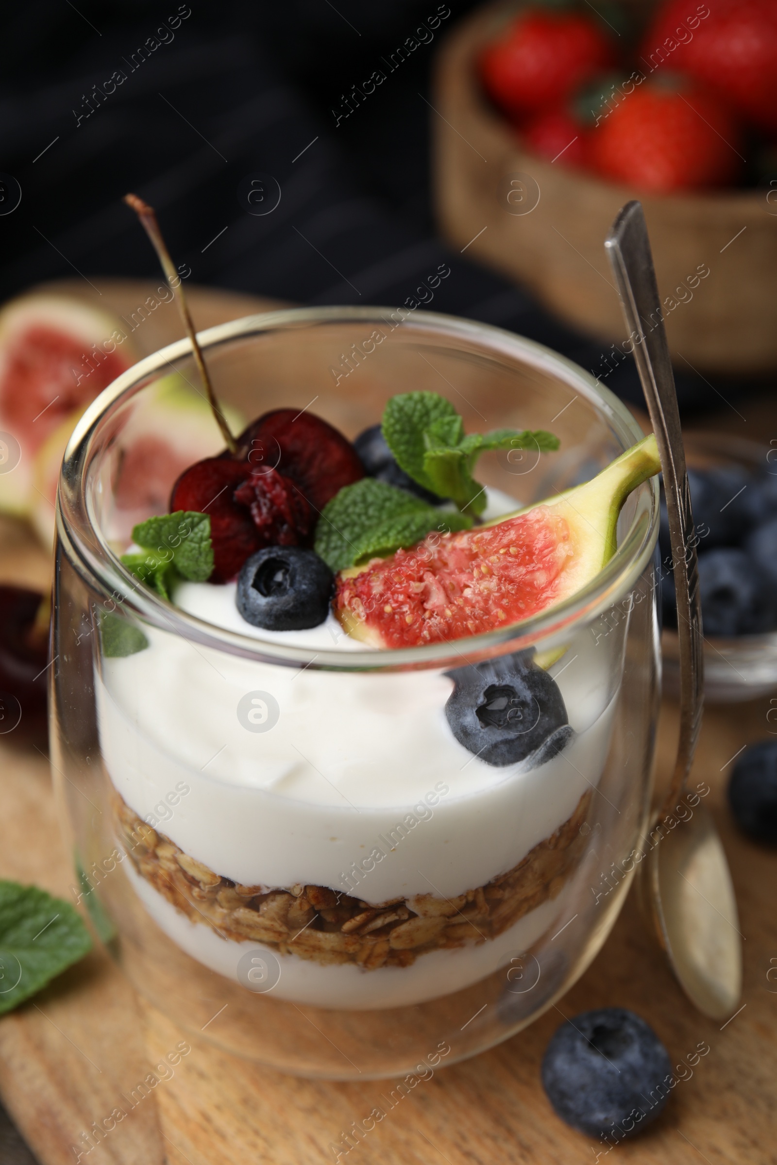 Photo of Glass with yogurt, berries, mint and granola on wooden table, closeup