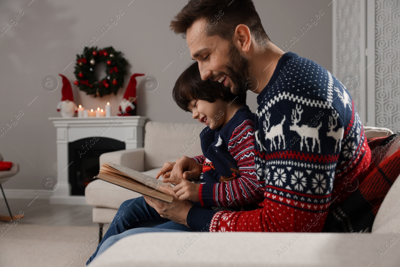 Photo of Father with his cute son reading book in room decorated for Christmas