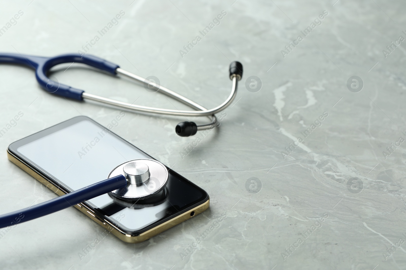 Photo of Modern smartphone and stethoscope on grey table. Space for text
