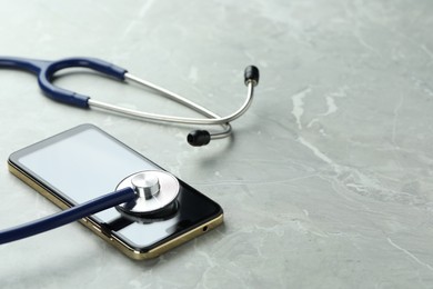 Modern smartphone and stethoscope on grey table. Space for text