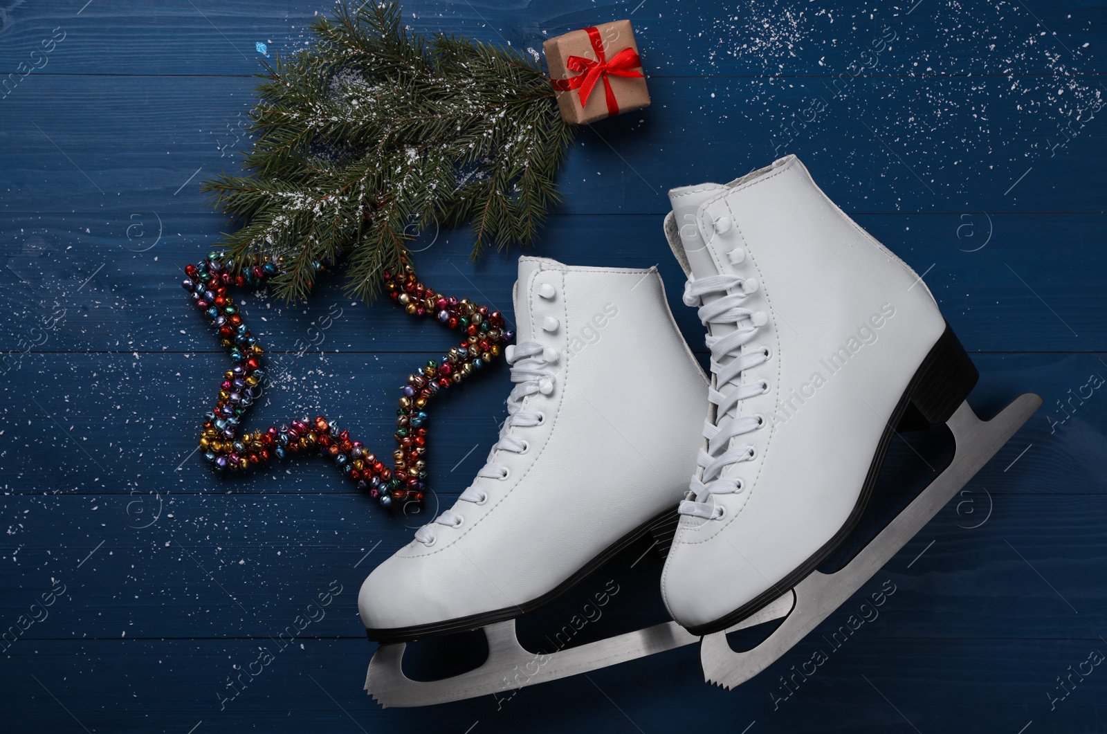 Photo of Pair of ice skates with Christmas decor on blue wooden background, flat lay