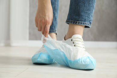 Woman wearing blue shoe covers onto her sneakers indoors, closeup