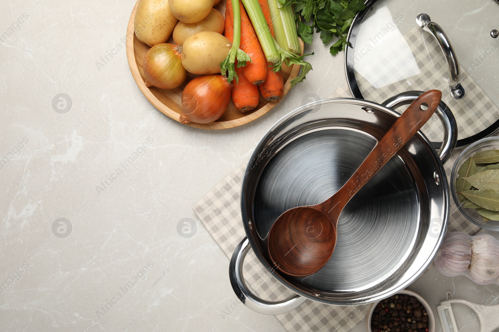 Photo of Pot with ladle and different ingredients for cooking tasty bouillon on light table, flat lay. Space for text