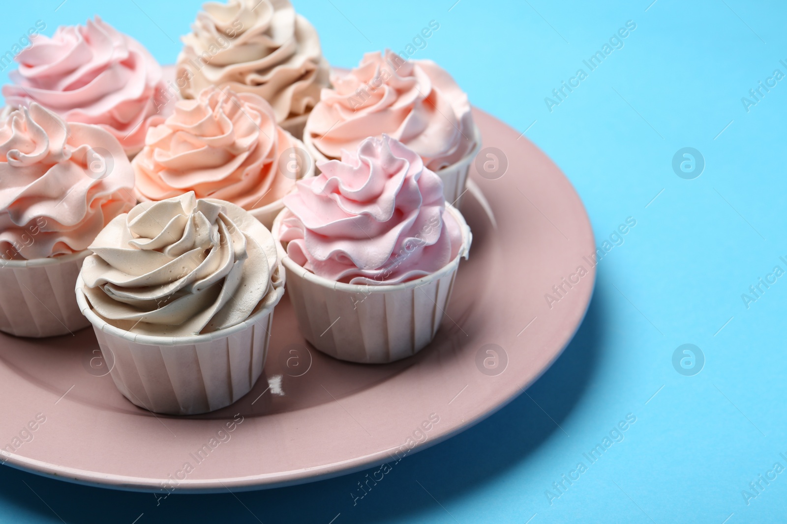 Photo of Plate with tasty cupcakes on light blue background, closeup