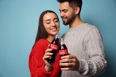 MYKOLAIV, UKRAINE - JANUARY 27, 2021: Young couple holding bottles of Coca-Cola against light blue background, focus on hands