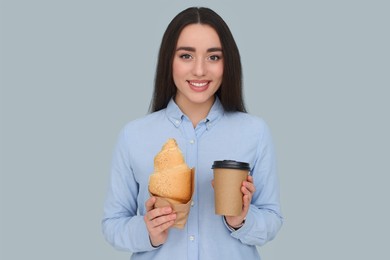 Photo of Young female intern with croissant and cup of drink on grey background