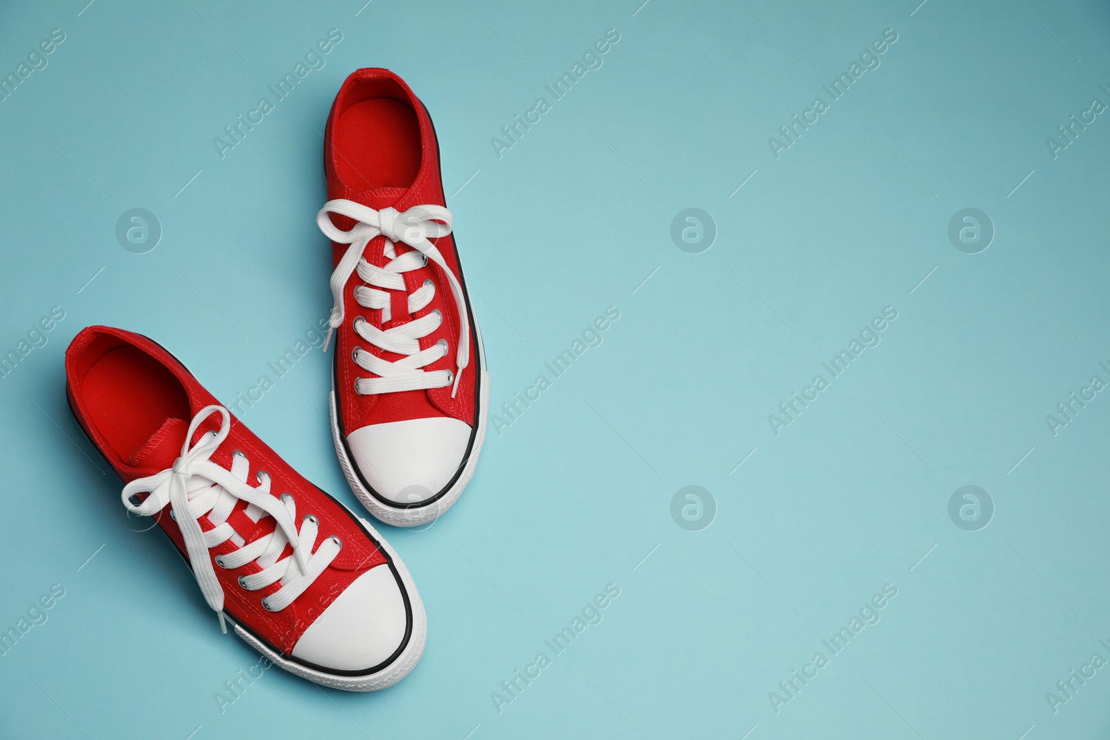 Photo of Pair of red classic old school sneakers on light blue background, flat lay. Space for text