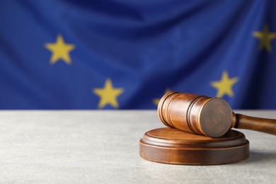 Photo of Wooden judge's gavel on grey table against European Union flag. Space for text