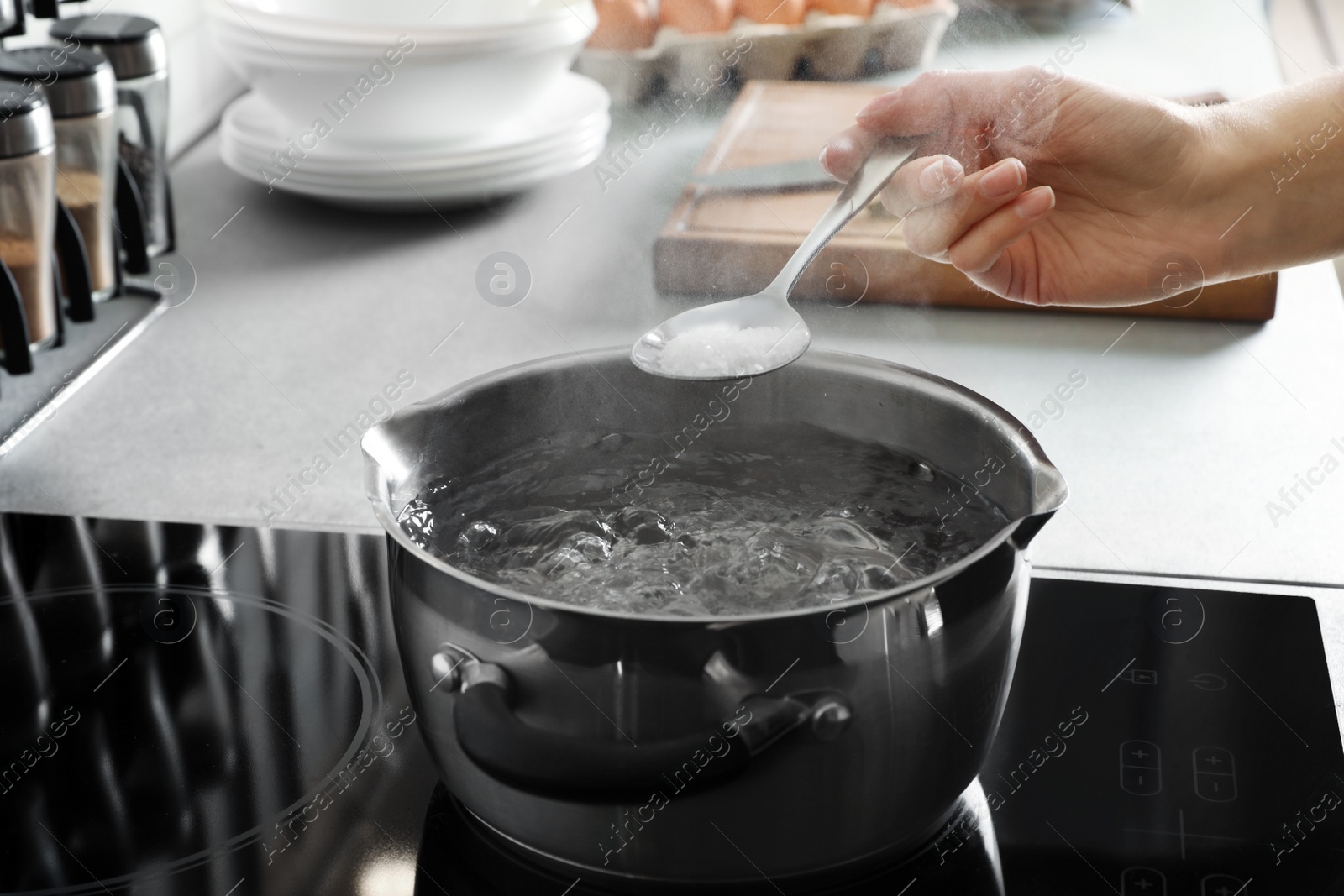 Photo of Woman salting boiling water in pot on stove, closeup