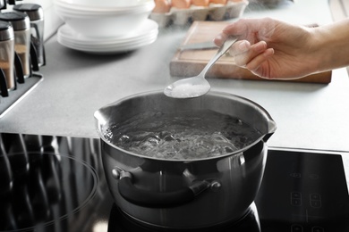 Woman salting boiling water in pot on stove, closeup