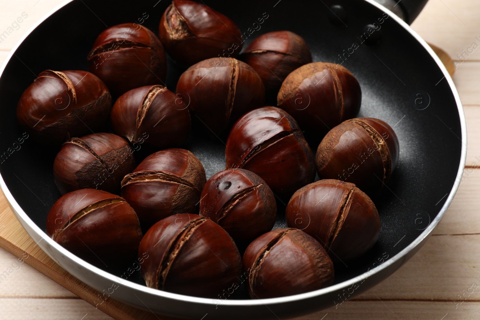 Photo of Roasted edible sweet chestnuts in frying pan on wooden table, closeup