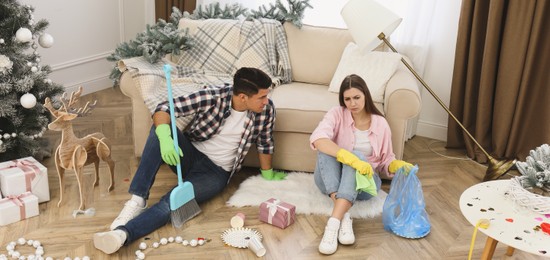 Image of Tired couple sitting in messy room while cleaning after New Year party. Banner design
