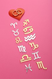 Zodiac compatibility. Signs, wedding rings and red heart on pink background, above view