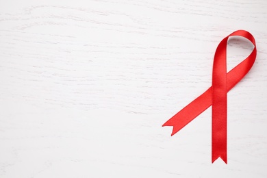 Photo of Top view of red ribbon on white wooden background, space for text. AIDS disease awareness