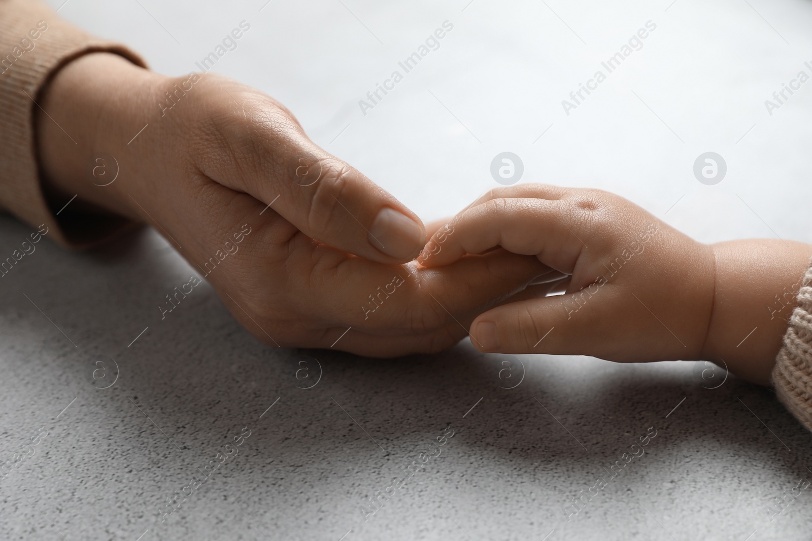 Photo of Woman holding hands with her little daughter at light grey table, closeup